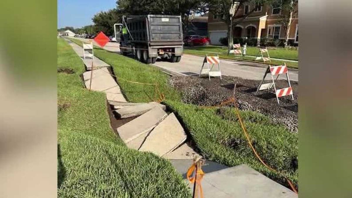 Trecho reparado da Cypress River Road em St. Cloud com palmeiras e casas ao fundo sob céu azul claro.
