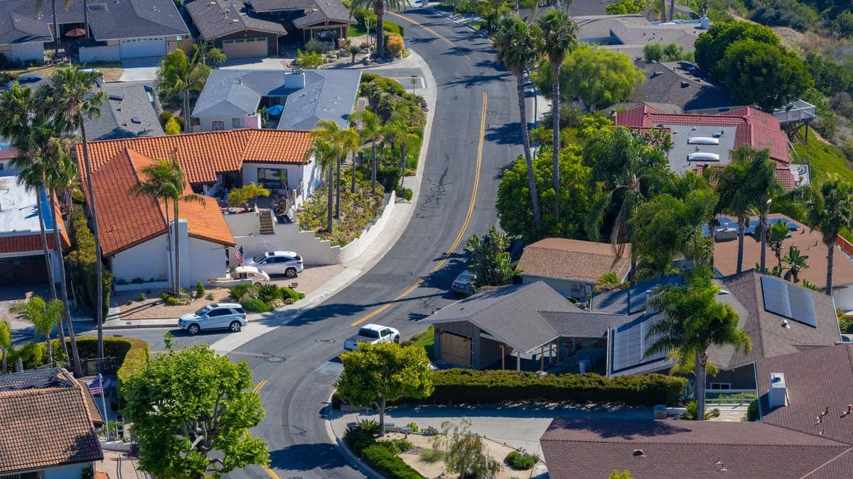 Vista aérea de um bairro residencial com várias casas, ruas e árvores ao redor em um dia ensolarado